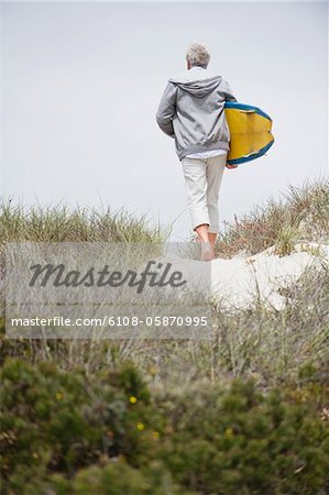 Rear view of a senior man carrying surfboard on the beach