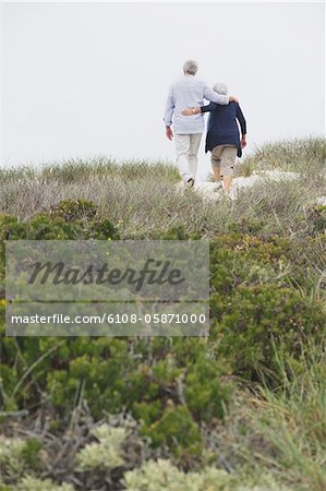 Rear view of a senior couple walking on the beach with their arms around each other