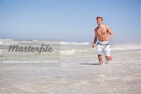 Mann läuft am Strand ohne Hemd