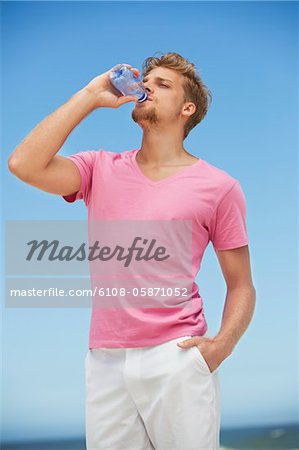 Junger Mann Wasser aus einer Flasche Wasser am Strand