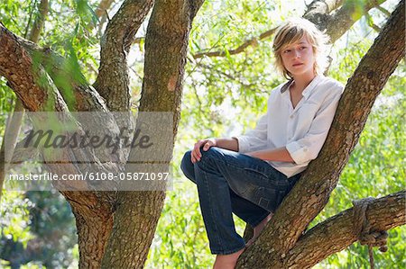 Contemplative little boy crouching on tree branch