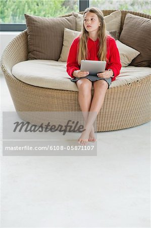 Fille assise dans un canapé en osier, en utilisant une tablette numérique