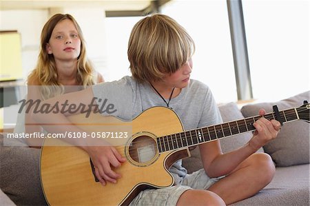 Adolescent joue une guitare avec sa soeur debout derrière lui à l'écoute