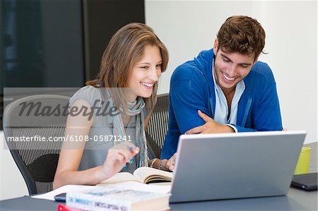 University students smiling while using laptop in classroom