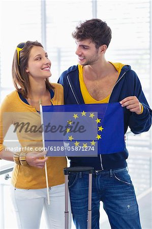 Couple holding European union flag at an airport and looking at each other