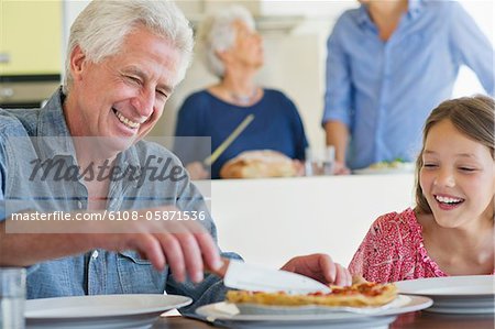 Man cutting cake with a knife and his granddaughter sitting near him