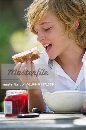 Little boy eating bread with jam outdoors