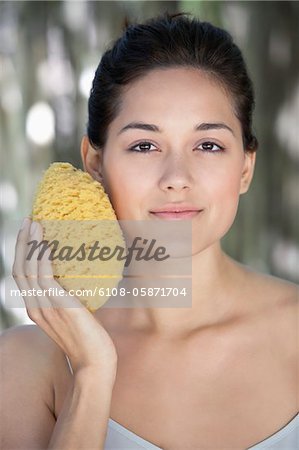 Beautiful young woman holding a bath sponge on her face