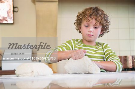 Cute little boy kneading dough at kitchen