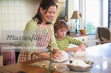 Grandmother and little boy kneading dough at kitchen