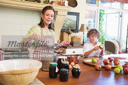 Grandmother cooking food and little boy peeling an apple at home
