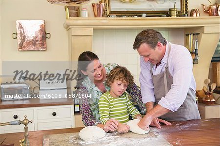 Netter kleiner Junge und seine Eltern kneten Teig in Küche