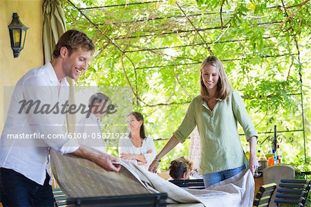 Couple placing tablecloth with family in the background