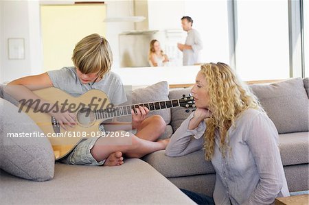 Teenage boy playing a guitar and his mother listening