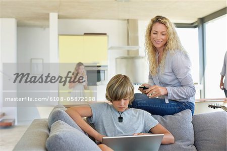 Teenage boy using a laptop and his mother looking at him