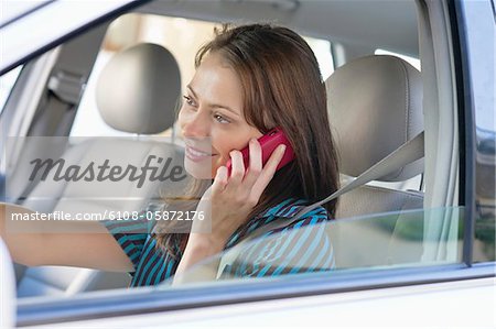 Beautiful young woman talking over mobile phone while driving a car