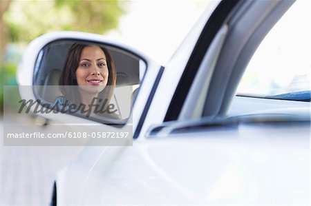 Reflection of a smiling young woman on a car side mirror