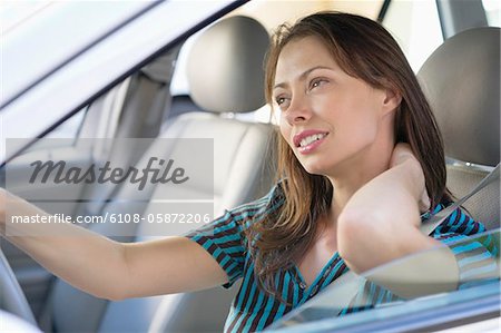 Tired young woman rubbing back of neck while driving a car