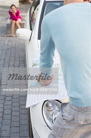 Rear view of a man looking at map on car with young woman sitting in the background