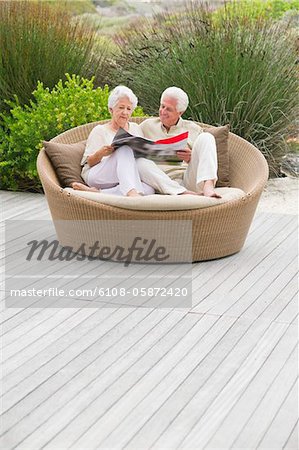 Senior couple assis dans un canapé en osier, lire un magazine