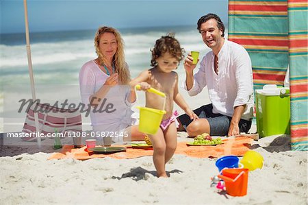 Girl playing on the beach with her parents sitting behind her