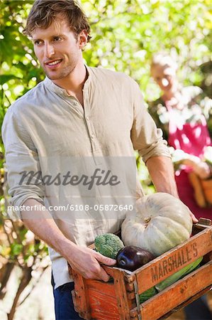 Homme tenant un cageot de légumes souriant