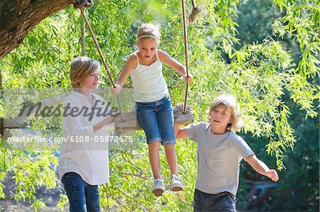 Smiling little siblings playing in tree swing