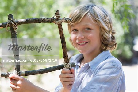 Portrait of a cute little boy holding frame of driftwood outdoors