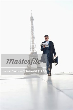 Homme d'affaires marchant avec mallette, lecture de journaux avec la tour Eiffel en arrière-plan, Paris, Ile-de-France, France