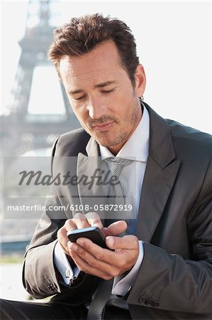 Homme d'affaires à l'aide d'un téléphone mobile avec la tour Eiffel en arrière-plan, Paris, Ile-de-France, France