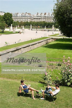 Homme utilisant un ordinateur portable avec une femme lisant un magazine dans le jardin, Jardin des Tuileries, Paris, Ile-de-France, France