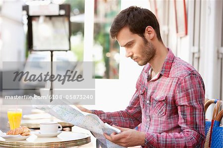 Man sitting at a sidewalk cafe and reading a map, Paris, Ile-de-France, France