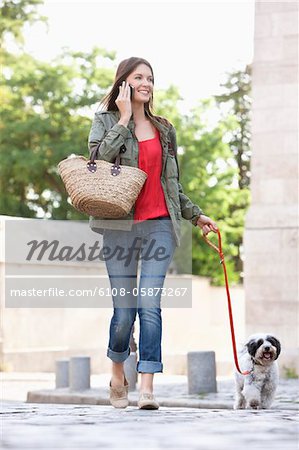 Femme tenant un chiot en laisse tout en parlant sur un téléphone mobile, Paris, Ile-de-France, France