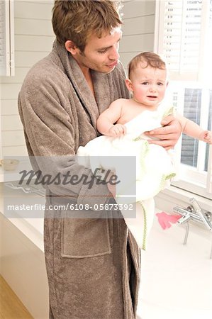 Young man in bathrobe with baby in bathroom