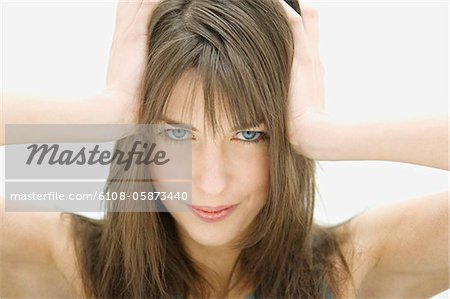 Portrait d'une jeune femme regardant la caméra, les mains sur la tête