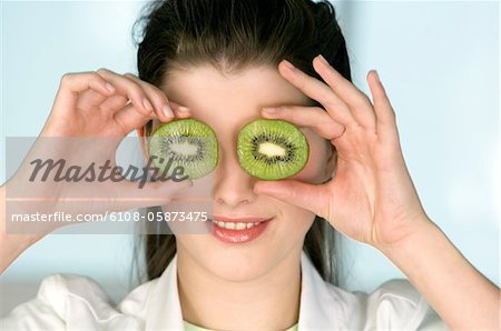Portrait of a young smiling woman covering her eyes with 2 halves of kiwi fruit