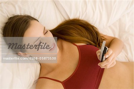 Portrait of a young woman lying on a bed, holding her cell