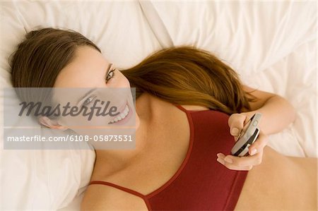 Portrait of a young woman lying on a bed, holding her cell