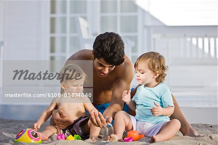 Man playing with his son and daughter in sand