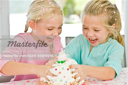 Two girls playfully inserting their hands in a birthday cake