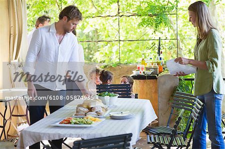 Couple arranging food on dining table with family in the background