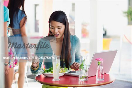 Beautiful woman eating food with laptop on table in a restaurant
