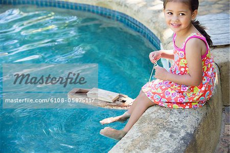 Girl sitting at edge of swimming pool with toy boat in water