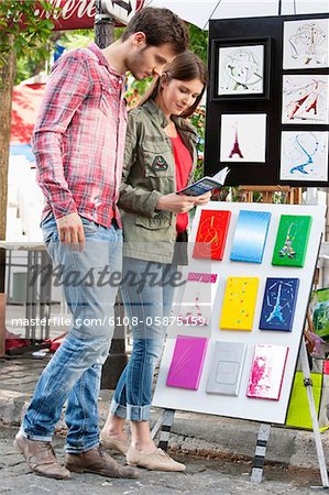 Couple à la recherche de cartes postales de la tour Eiffel à un étal de marché, Paris, Ile-de-France, France