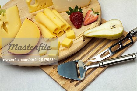 A set of different cheeses, strawberry, pear and special cheese knives on a wooden board