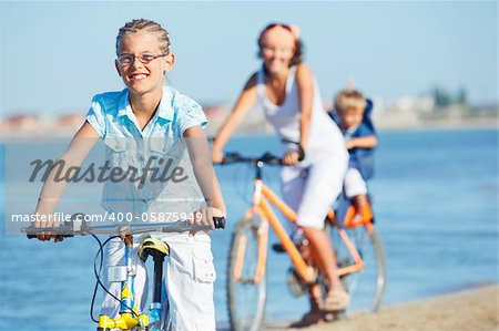 Cute girl with her mother and brother ride bikes along the beach. Focus on girl