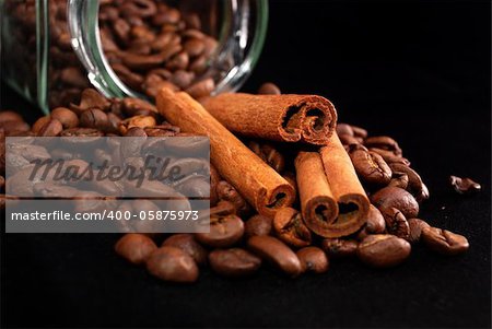 Brown fried grains of coffee and stick cinnamon scattered on a black background