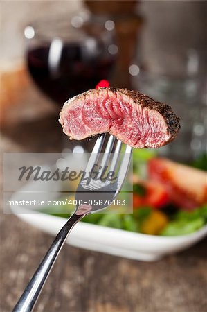 slice of a steak on a fork over salad
