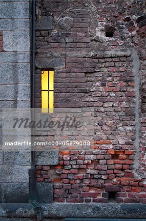 Ancient brick wall with small lit window