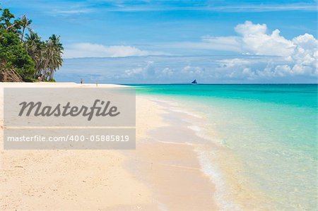 tropical white beach with a sailing boat at the horizon